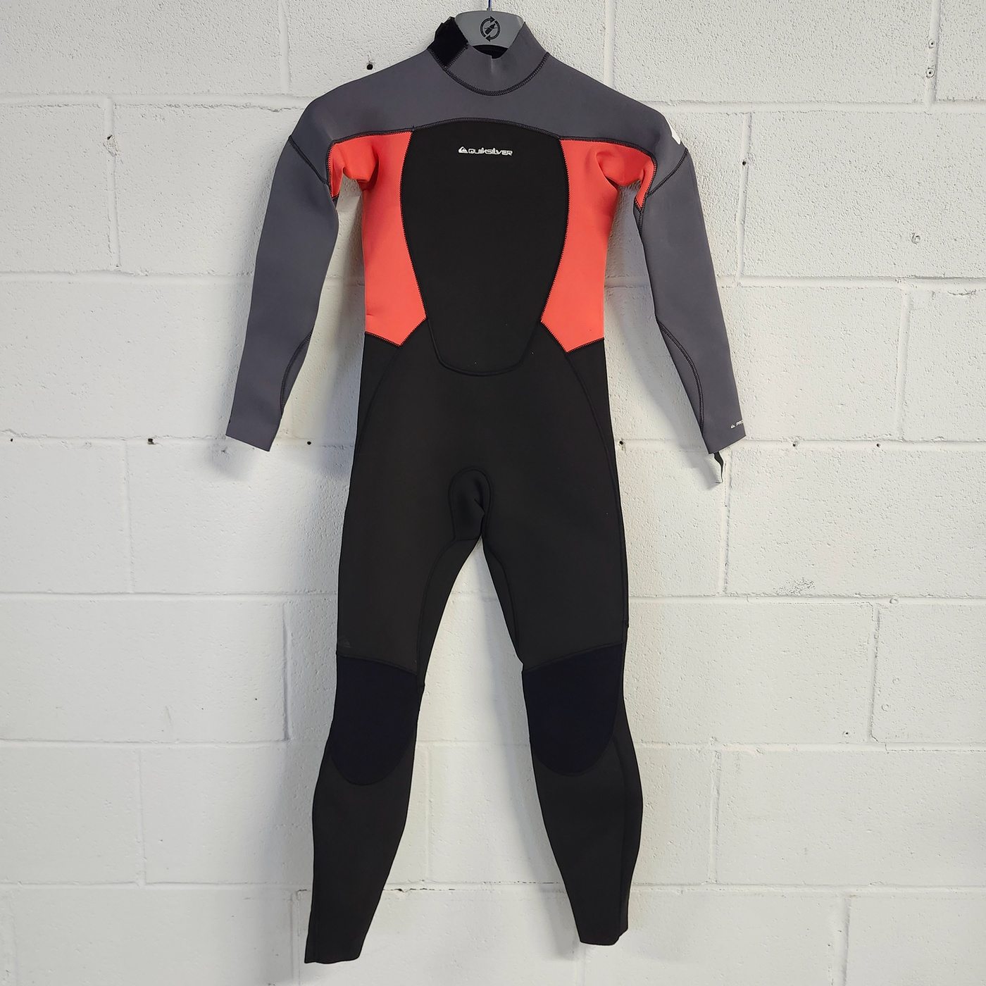Wetsuit with gray, red, and black sections on a white tiled floor