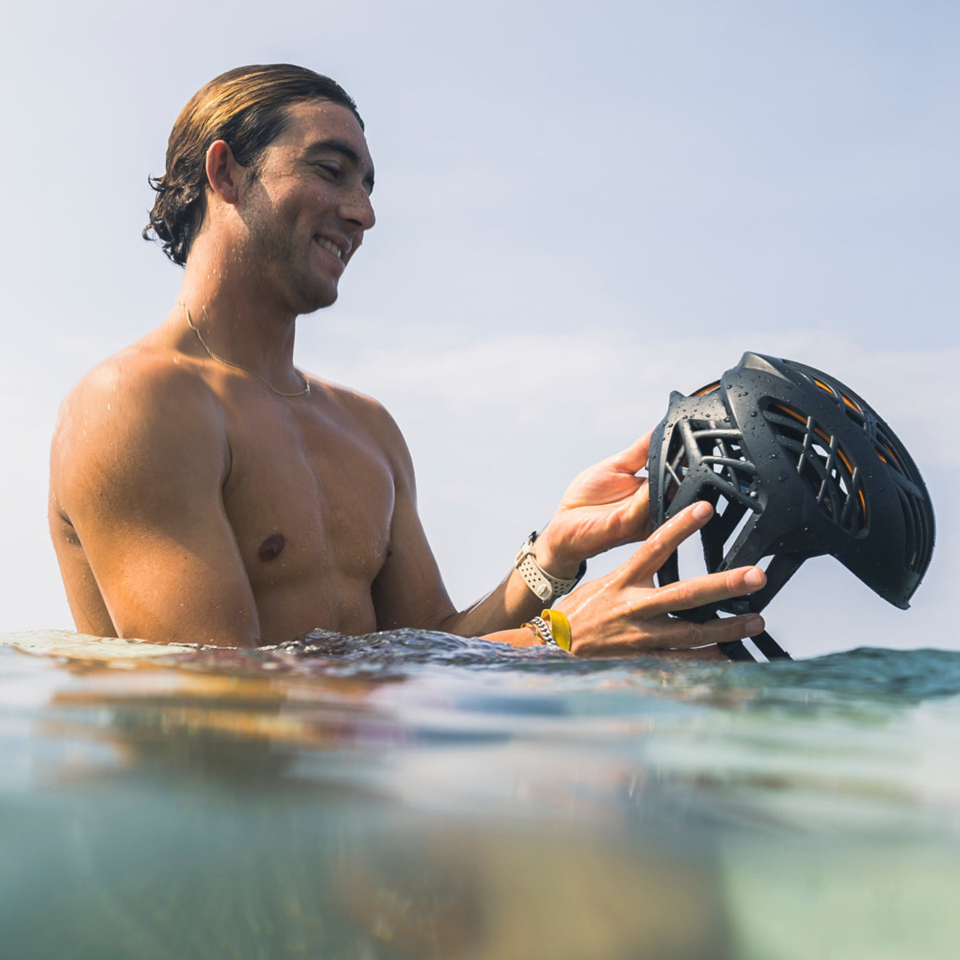 
                  
                    Man holding a black helmet in the water with a clear sky background
                  
                