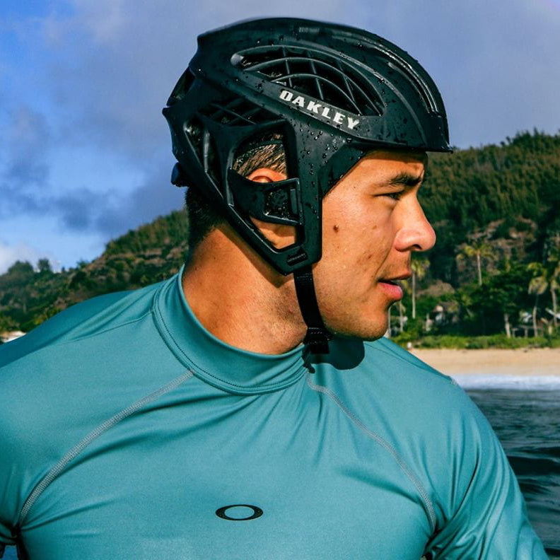 
                  
                    Person wearing a teal wetsuit and black Oakley helmet by a body of water with mountains in the background.
                  
                